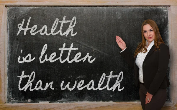 Teacher showing Health is better than wealth on blackboard — Stock Photo, Image