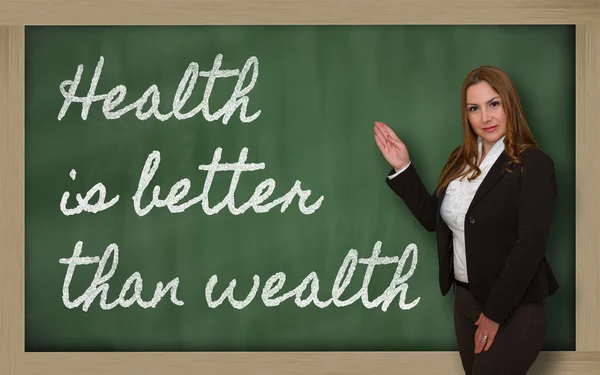 Teacher showing Health is better than wealth on blackboard — Stock Photo, Image