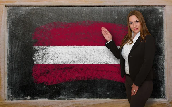 Teacher showing flag ofLatvia on blackboard for presentation mar — Stock Photo, Image