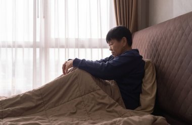 Bunalımlı, yaşlı, Asyalı, bunalımlı bir kadın. İnsanlar sabahın erken saatlerinde yatak odasındaki pencerelerle yatakta oturuyor. Karantina yaşam tarzı. Mutsuz bir hayat.