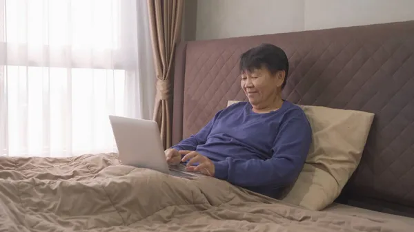 나이든 아시아 집에서 일하고 컴퓨터 노트북 키보드로 타이핑하는 사람들 침대에서 — 스톡 사진
