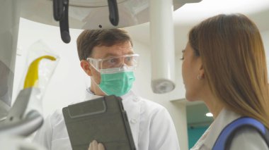 Kafkasyalı bir dişçi, insanlar dişçi röntgenini tablet teknolojisiyle hasta kadına gösteriyor. Diş muayenesi. Doktor bey. Diş sağlığı, sağlık ve diş sağlığı.