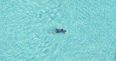 Yaz mevsiminde temiz su dalgalarıyla mavi ya da turkuaz yüzme havuzunda yüzen bir adamın havadan görünüşü. Tatilde insanların yaşam tarzı.