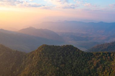 Orman ağaçlarının ve sisli, bulutlu yeşil dağ tepelerinin havadan görünüşü. Doğa manzarası arka planı, Tayland.