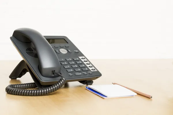 Telefone na mesa com bloco de notas na mesa de madeira — Fotografia de Stock