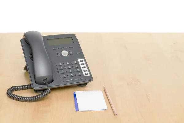 Teléfono en el escritorio con bloc de notas en escritorio de madera — Foto de Stock