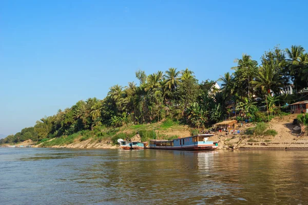 ロングテールボート ヤシの木や家地元の人々と川沿いに表示されます メコン川 ルアンパバーン ラオス — ストック写真