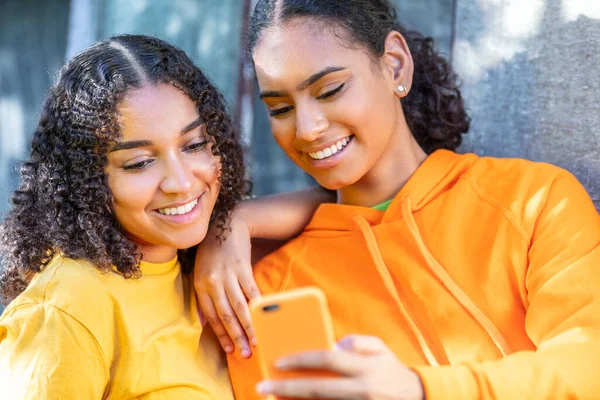 幸せな笑顔かなり混合レースアフリカ系アメリカ人ティーンの女の子女性若いです女性のための彼らのスマートフォンを使用してソーシャルメディア外 — ストック写真