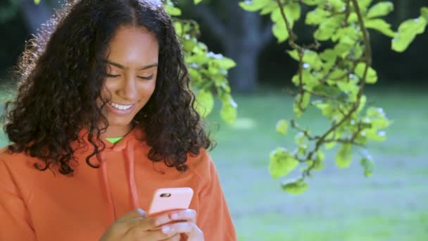 美しく 笑顔混合レースアフリカ系アメリカ人の女の子ティーン若いです屋外で彼女のスマートフォンや携帯電話を使用してソーシャルメディアやテキストメッセージ — ストック動画