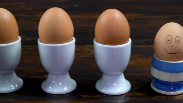 白い卵のカップにゆで卵の列に沿って一卵のストライプの卵のカップに幸せな笑顔が描かれているそれに描かれている — ストック動画