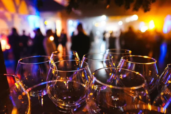 Las copas de vino en el resplandor de la luz sobre las siluetas borrosas de las personas de fondo Imagen de archivo