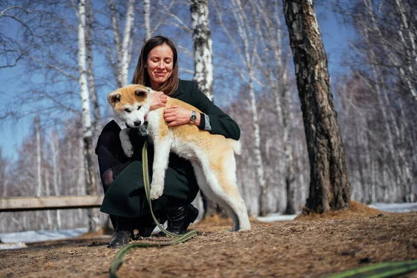 Mujer con abrigo oscuro abraza a un cachorro Akita Inu con correa verde larga en el parque de otoño Fotos de stock libres de derechos
