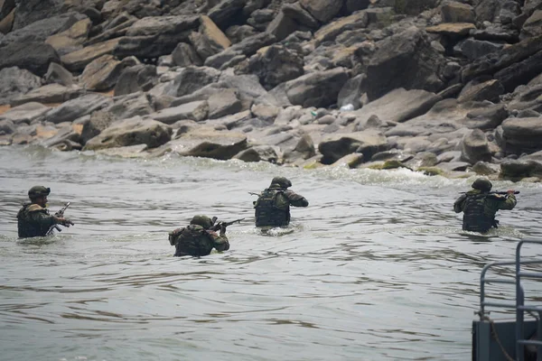 Cuatro soldados con uniformes militares salen del agua a la orilla Fotos de stock libres de derechos