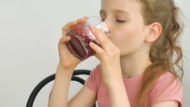 Gadis kecil yang manis meminum smoothie raspberry dan tersenyum. Minuman vegetarian. Potret close-up seorang anak yang menikmati jus raspberry lezat yang menyegarkan, makanan sehat — Stok Video