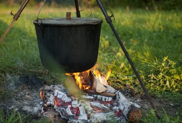 Mörk stor gryta eller gryta, kokpanna med kokande vatten inne ovanför brasan någonstans i parken eller bergen, campingkoncept Stockbild