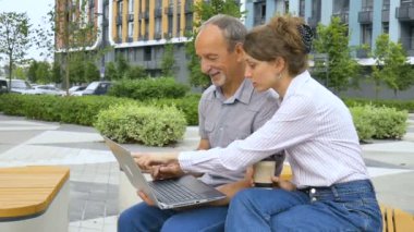 Genç çalışan, iş arkadaşına bilgisayar ve kurumsal yazılımın nasıl kullanılacağını öğretiyor. Ofis dışındaki bankta oturuyor. Koordine intership, eğitim ortaklığı..