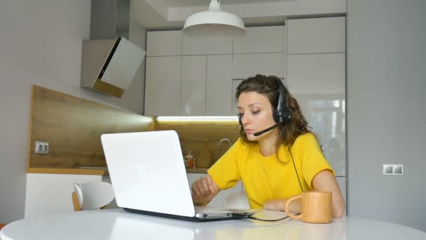 年轻女性正在使用笔记本电脑举行在线会议，一位带着数码平板电脑的女商人坐在她公寓的厨房里，账户经理，在户外工作，从事远程工作，提供支持 — 图库视频影像