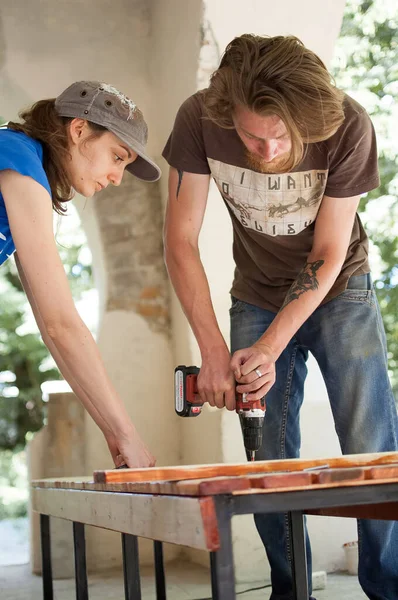 13.08.2021 - Ucraina, Goshcha, gruppo di giovani lavoratori utilizza cacciavite di potenza di perforazione, martello durante la costruzione banco di legno, farlo insieme — Foto Stock
