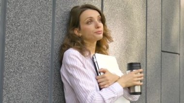 Gümüş dizüstü bilgisayarı ve kahve fincanı olan genç bir kadının portresi. Sabah koyu gri duvarın yanında toplantı bekliyor. Uzaktan çalışma, kahve molası, zeki öğrenci konsepti.