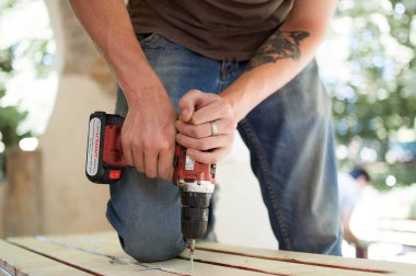 Ukrayna, Goshcha, gönüllü etkinlik, - Ağustos, 2021 - yetenekli genç erkek işçi inşaat ahşap tezgahı boyunca tornavida sondajı kullanıyor, kendin yap.