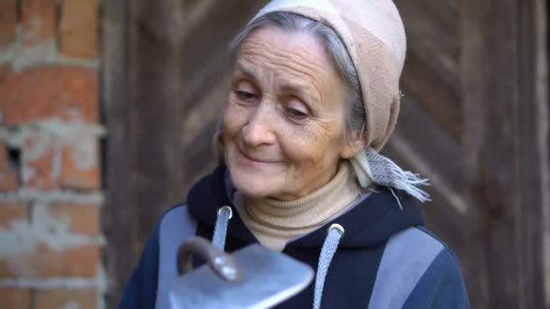 Счастливая красивая пожилая женщина держит металлическую мотыгу и убирает ее после работы и прополки в саду, счастливая пенсия — стоковое видео