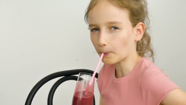 Dulce niña bebe batido de frambuesa y sonríe. Bebida vegetariana. Retrato de cerca de un niño que disfruta de un refrescante jugo de frambuesa sabroso, alimentación saludable — Vídeos de Stock