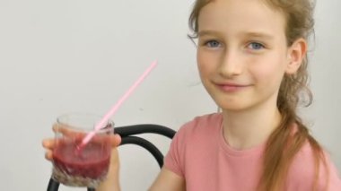 Tatlı küçük kız ahududu kokteyli içip gülümsüyor. Vejetaryen içeceği. Taze ahududu suyu ve sağlıklı beslenmeyi seven bir çocuğun yakın plan portresi.