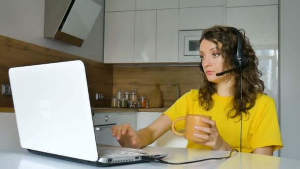 Молодая женщина проводит онлайн-встречу с помощью ноутбука, деловая женщина с цифровым планшетом сидит на кухне в своей квартире, менеджер по работе с клиентами, работает на открытом воздухе, удаленная работа, поддержка — стоковое видео