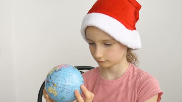 Földrajzi nevekkel ellátott földgömböt ukrán cirill betűkkel egy szőke lány tartja télapó kalapban. Emberi felelősség, környezetbarát, új év, karácsonyi ünnepség előkészítése — Stock videók