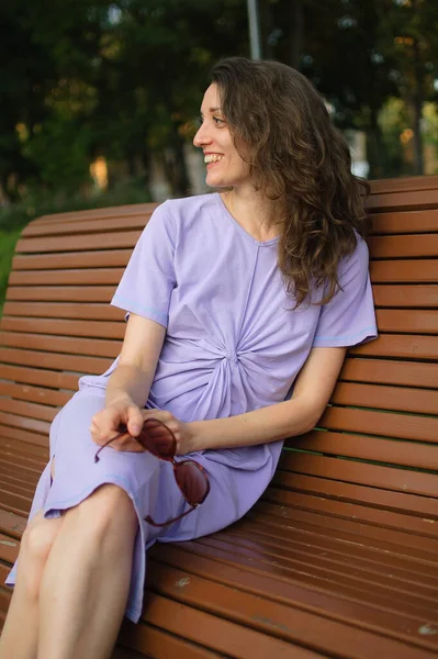 Chica joven en vestido violeta claro está teniendo gran tiempo durante las vacaciones en el verano sentado en el banco, concepto de viaje —  Fotos de Stock