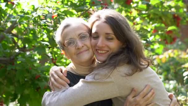 Gelukkig senior moeder in bril is knuffelen haar volwassen dochter, de vrouwen genieten samen, oprechte familie van verschillende leeftijden generaties plezier buiten — Stockvideo