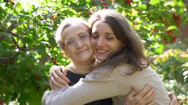 Šťastná starší matka v brýlích objímá svou dospělou dceru, ženy si spolu užívají, upřímná rodina různých věkových generací se baví venku