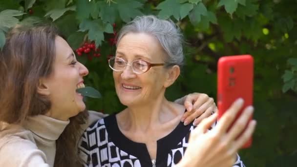 Adult daughter and senior mum are taking self-portrait picture, selfie on red smartphone together, happy retirement, mothers day concepts. — Stock Video