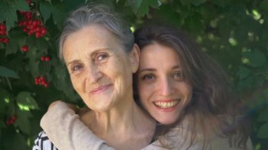 Gözlüklü mutlu kıdemli anne yetişkin kızına sarılıyor, kadınlar birlikte eğleniyor, farklı nesillerden gelen samimi aile dışarıda eğleniyor.