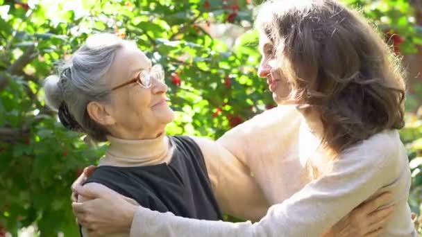 Gelukkig senior moeder in bril is knuffelen haar volwassen dochter, de vrouwen genieten samen, oprechte familie van verschillende leeftijden generaties plezier buiten — Stockvideo