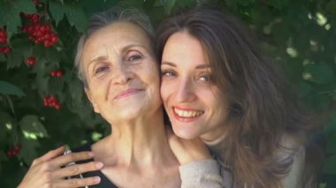 Gözlüklü mutlu kıdemli anne yetişkin kızına sarılıyor, kadınlar birlikte eğleniyor, farklı nesillerden gelen samimi aile dışarıda eğleniyor.