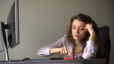Kıvırcık saçlı ve beyaz gömlekli yorgun genç kadın ofiste çalışıyor ve kırmızı akıllı telefonunu, rutin işini, serbest çalışmayı, tükenme sendromunu kullanıyor.