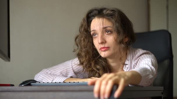 Giovane donna stanca con i capelli ricci e camicia bianca sta lavorando in ufficio utilizzando il suo computer portatile, lavoro di routine, freelance, sindrome di burnout — Video Stock