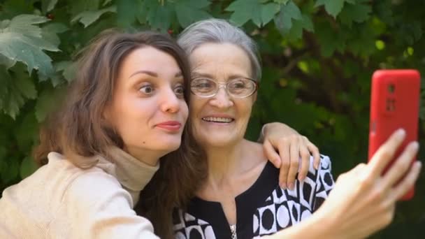 大人の娘とお母さんが自画像を撮り、赤いスマートフォンで自撮り、幸せな退職、母の日のコンセプト. — ストック動画