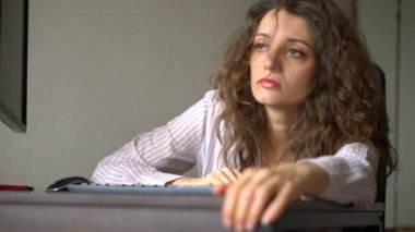 Kıvırcık saçlı ve beyaz gömlekli yorgun bir kadın ofiste çalışıyor. Dizüstü bilgisayarını, rutin işini, serbest çalışmayı, tükenme sendromunu kullanıyor.