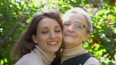 Gözlüklü mutlu kıdemli anne yetişkin kızına sarılıyor, kadınlar birlikte eğleniyor, farklı nesillerden gelen samimi aile dışarıda eğleniyor.