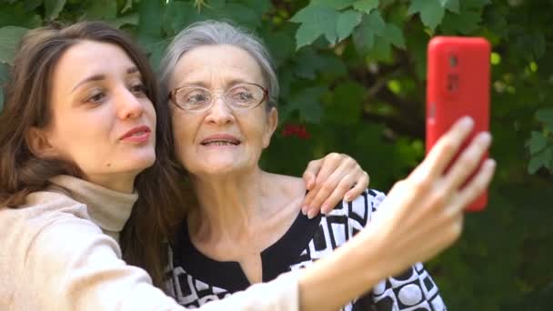 Fille adulte et maman aînée prennent une photo autoportrait, selfie sur smartphone rouge ensemble, retraite heureuse, concepts de la fête des mères. — Video