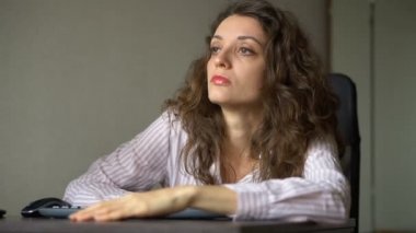 Kıvırcık saçlı ve beyaz gömlekli yorgun bir kadın ofiste çalışıyor. Dizüstü bilgisayarını, rutin işini, serbest çalışmayı, tükenme sendromunu kullanıyor.