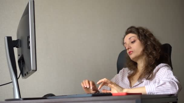 Νεαρή γυναίκα διευθυντής γραφείου σε λευκό πουκάμισο και σγουρά μαλλιά κάθεται στο τραπέζι και πληκτρολογώντας χρησιμοποιώντας πληκτρολόγιο, εργασία ρουτίνας, freelance. — Αρχείο Βίντεο