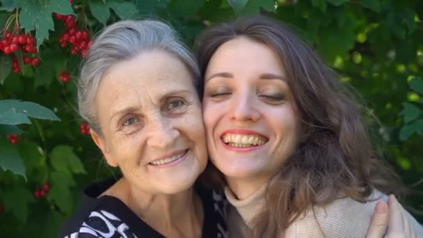 Szczęśliwa starsza matka w okularach przytula swoją dorosłą córkę, kobiety cieszą się razem, szczera rodzina w różnym wieku bawiąc się na świeżym powietrzu — Wideo stockowe