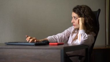 Kıvırcık saçlı ve beyaz gömlekli yorgun genç bir kadın ofiste bilgisayarla çalışıyor, kırmızı topuklu ayakkabılarıyla masada oturuyor, rutin işler, serbest çalışma, tükenme sendromu