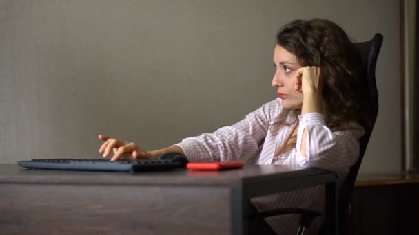 Mujer joven y cansada con el pelo rizado y camisa blanca está trabajando en la oficina con su ordenador, sentado con las piernas en tacones altos rojos en la mesa, el trabajo de rutina, freelance, síndrome de burnout — Vídeo de stock