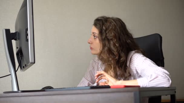 Νεαρή γυναίκα διευθυντής γραφείου σε λευκό πουκάμισο και σγουρά μαλλιά κάθεται στο τραπέζι και πληκτρολογώντας χρησιμοποιώντας πληκτρολόγιο, εργασία ρουτίνας, επίλυση προβλημάτων, freelance. — Αρχείο Βίντεο