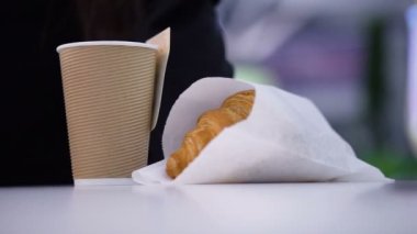 Lezzetli, taze kruvasanlar. Kağıt bardakta kahve, bulanık arka planda kadınların elinde..