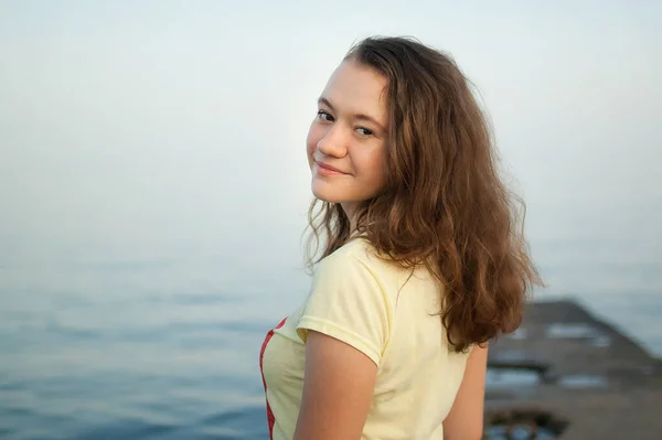 Ung flicka i gul t-shirt på havet och blå himmel bakgrund, sommar, resor, kvinnliga porträttbegrepp Stockfoto